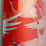 Close up photo of the front of the pillow showing a woven red stripe textile with flying cranes in white and gold thread. Repurposed wedding kimono silk.