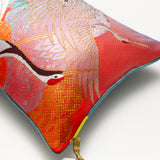 red oriental pillow detail of one corner. Cranes head in red and gold, other metallic cranes and a slight view of the blue velvet on the back of the pillow.