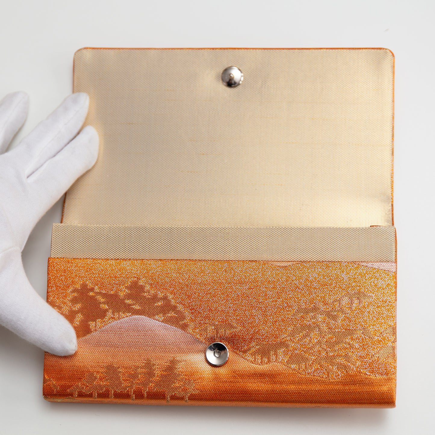 View of the metallic vintage Japanese clutch bag being held open by a gloved hand showing the gold silk lining and metal fastener.