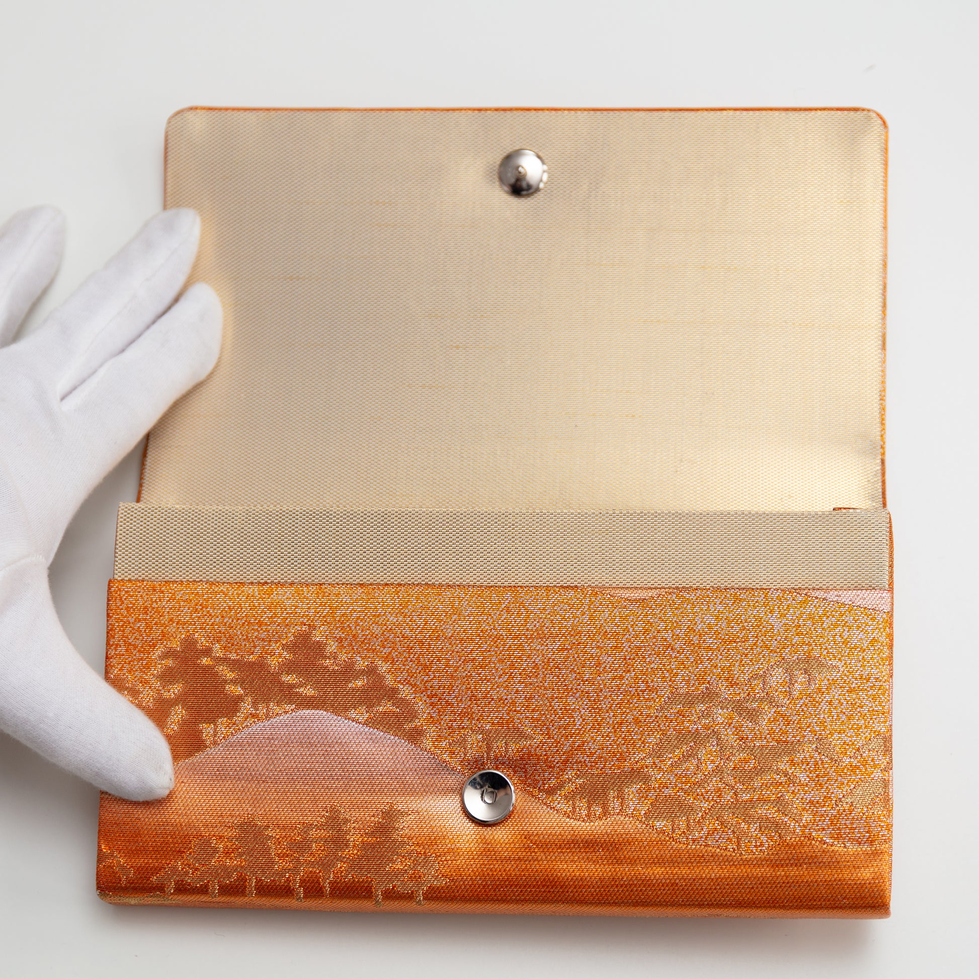 View of the metallic vintage Japanese clutch bag being held open by a gloved hand showing the gold silk lining and metal fastener.