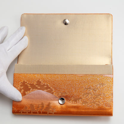 View of the metallic vintage Japanese clutch bag being held open by a gloved hand showing the gold silk lining and metal fastener.