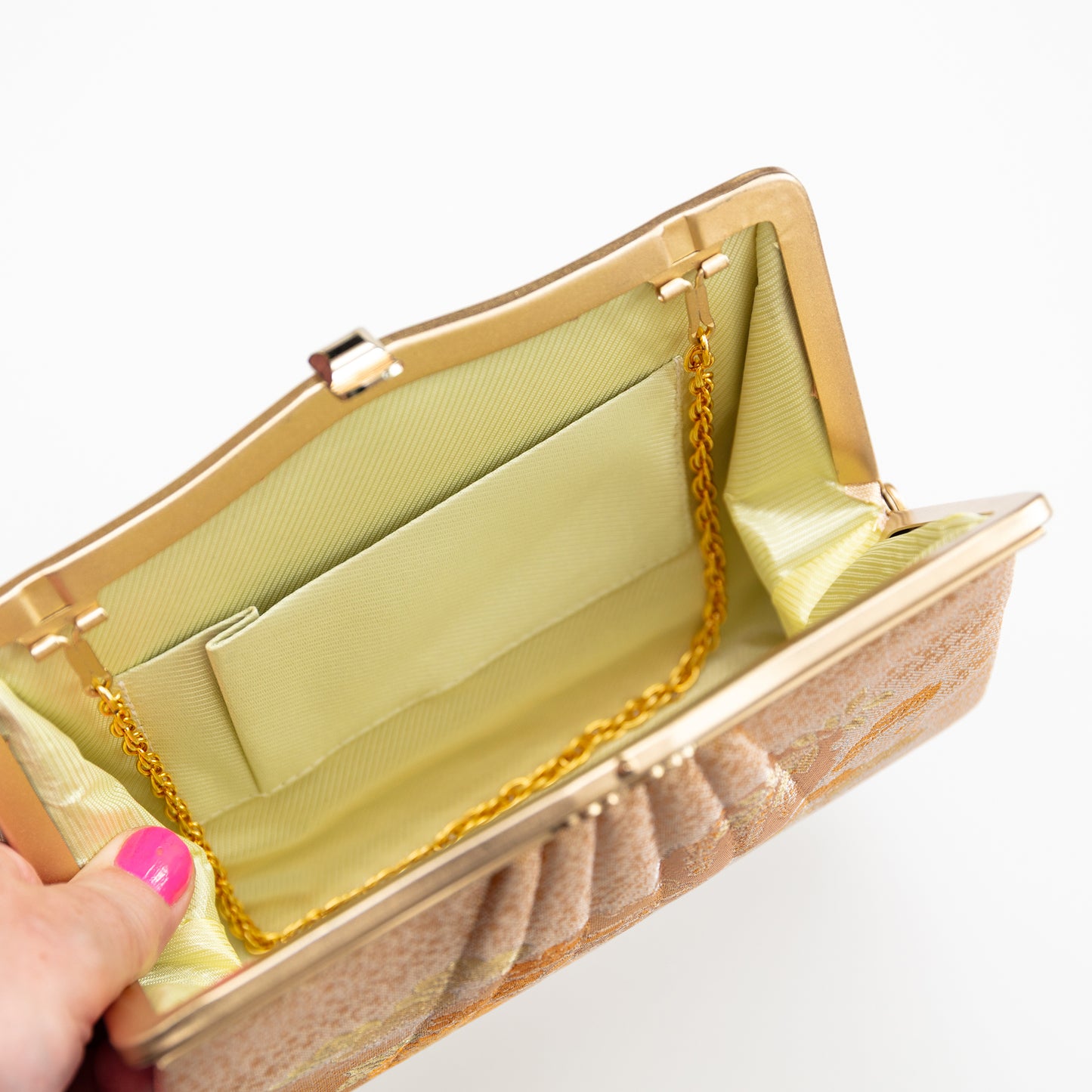 Gold clutch bag with a chain strap held by a hand on a white background. Strap can be tucked inside with convertible hinges.
