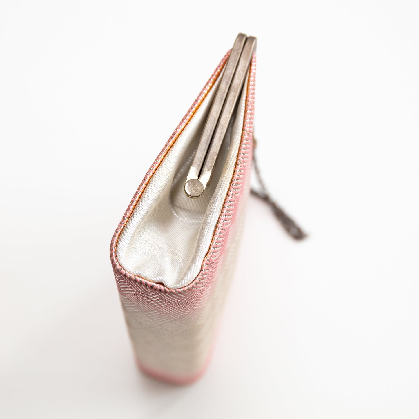 Close-up of a pink silk clutch bag with a white interior on a light gray background