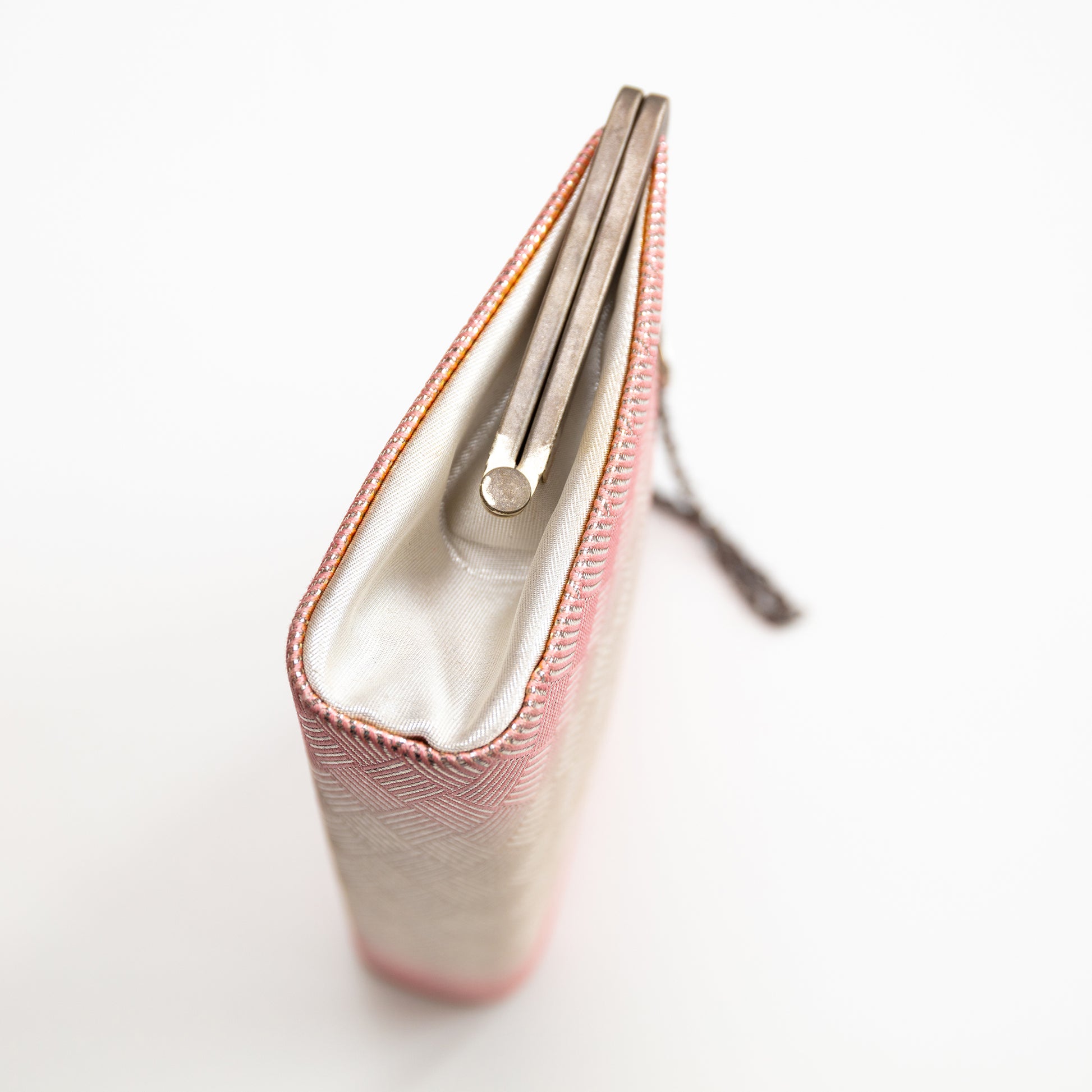 Close-up of a pink silk clutch bag with a white interior on a light gray background