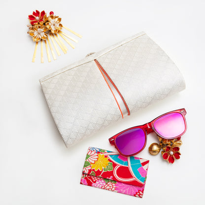 White silk vintage Japanese silver clutch bag with colourful sunglasses, floral cardholder, and decorative hairpin on a light background