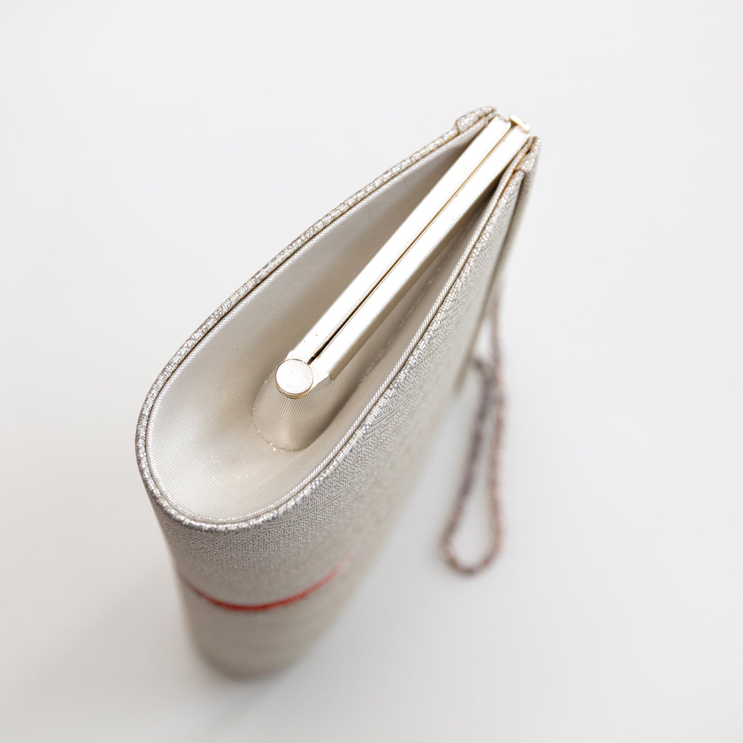 Side view of a silver clutch bag with a strap on a light gray background