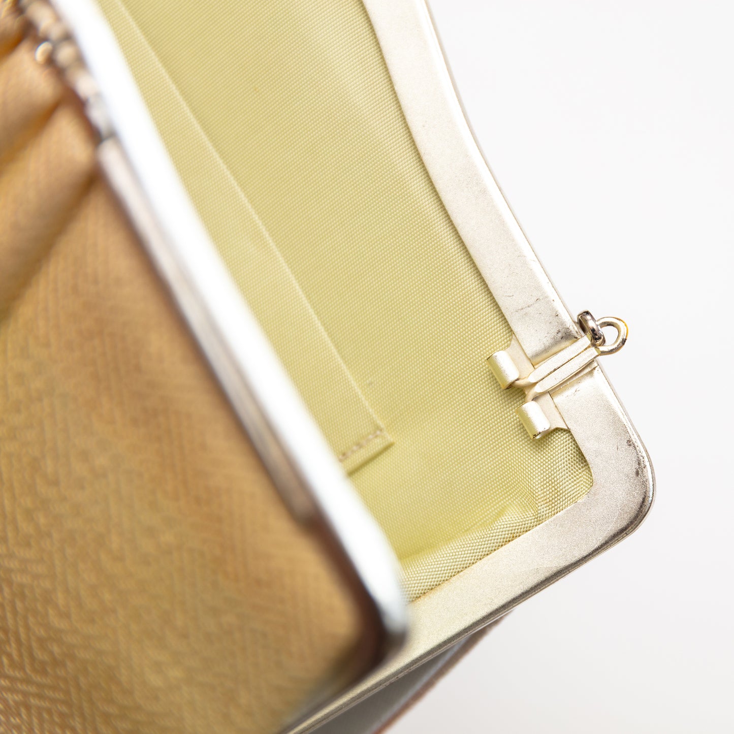 Close-up of a peach to cream silk 1950s clutch bag with a cream silk interior on a white background. The strap hinges tuck in or out.