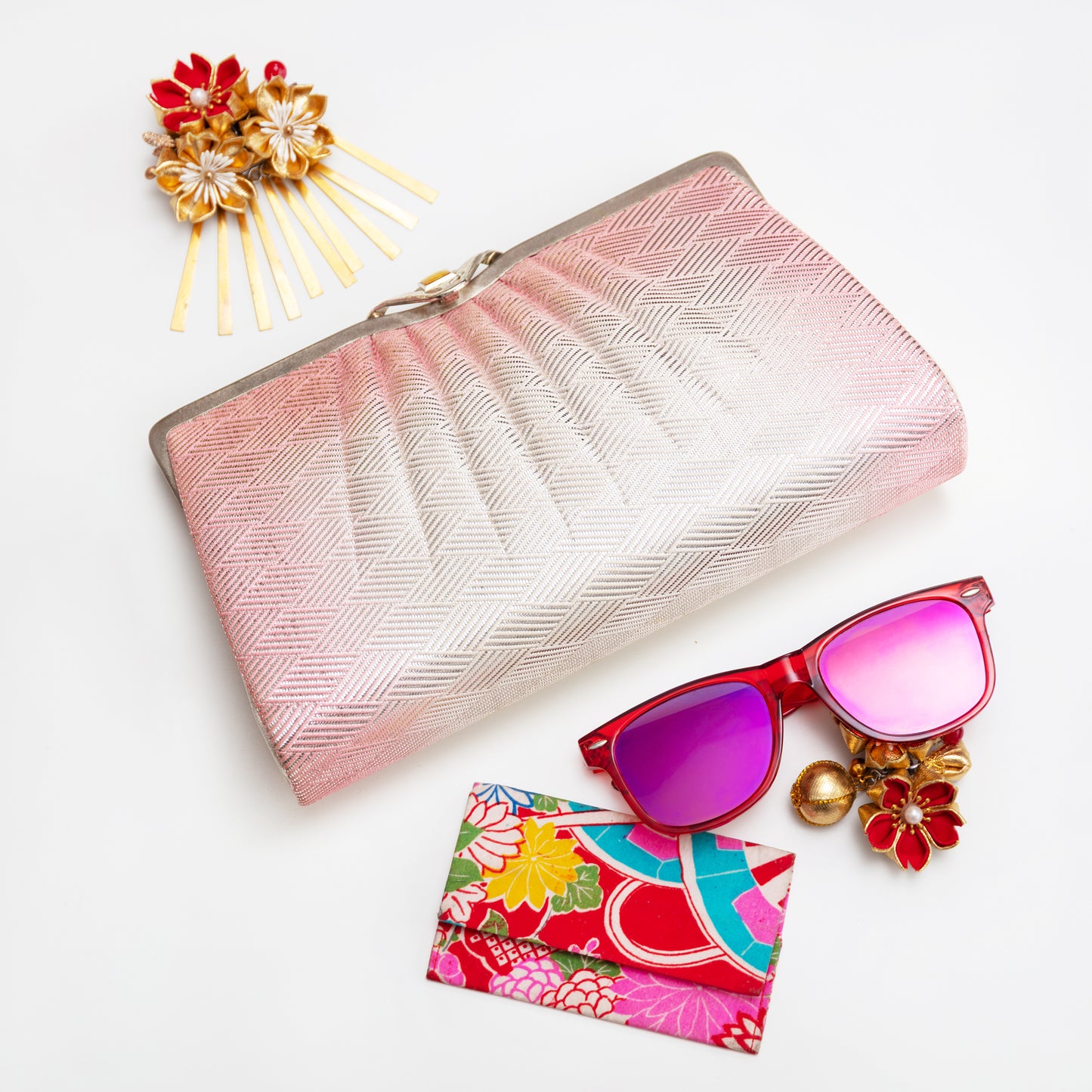 Pink clutch, sunglasses with colorful case, and decorative hair pins on a white background
