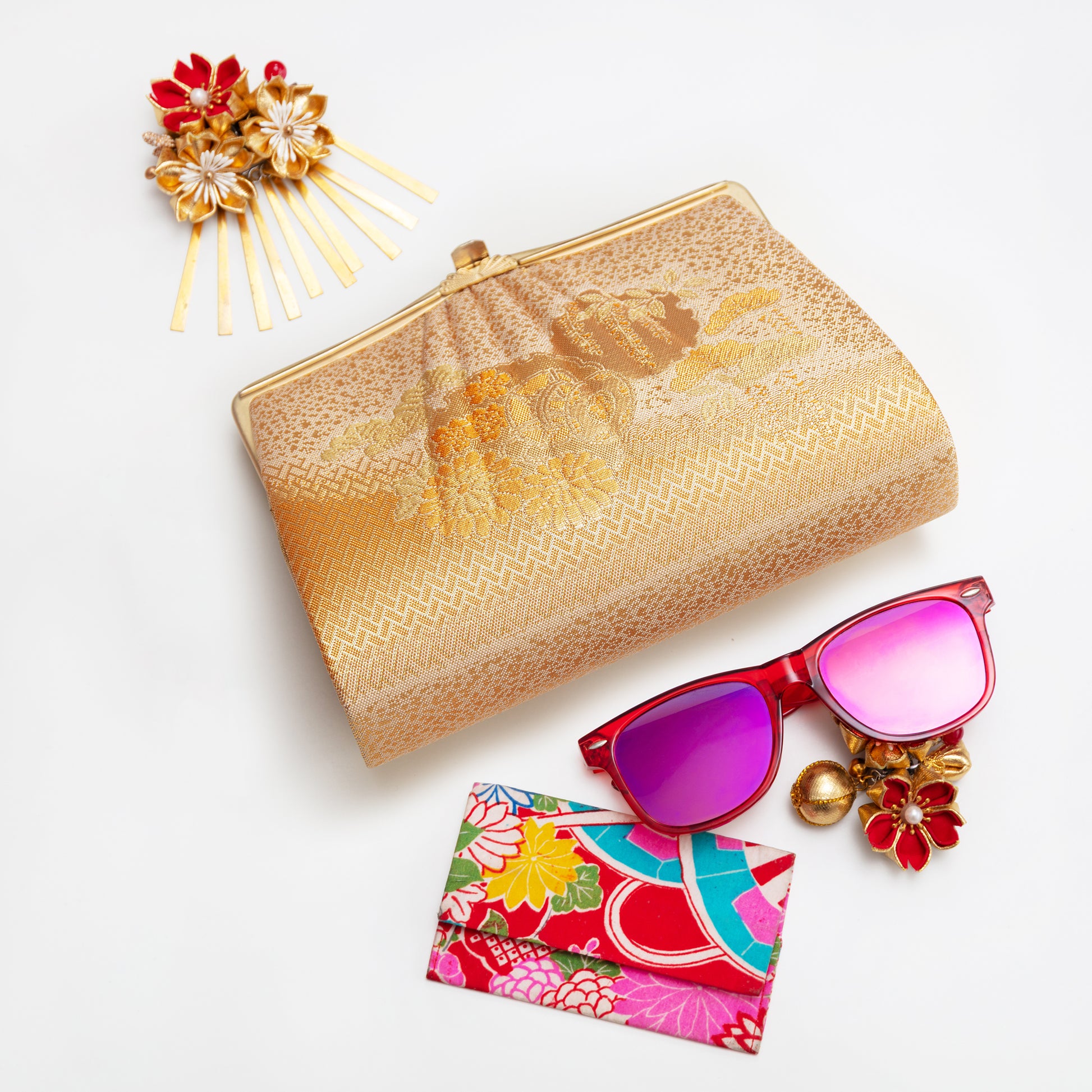Gold clutch, sunglasses with pink lenses, floral cardholder, and decorative hairpin on a white background