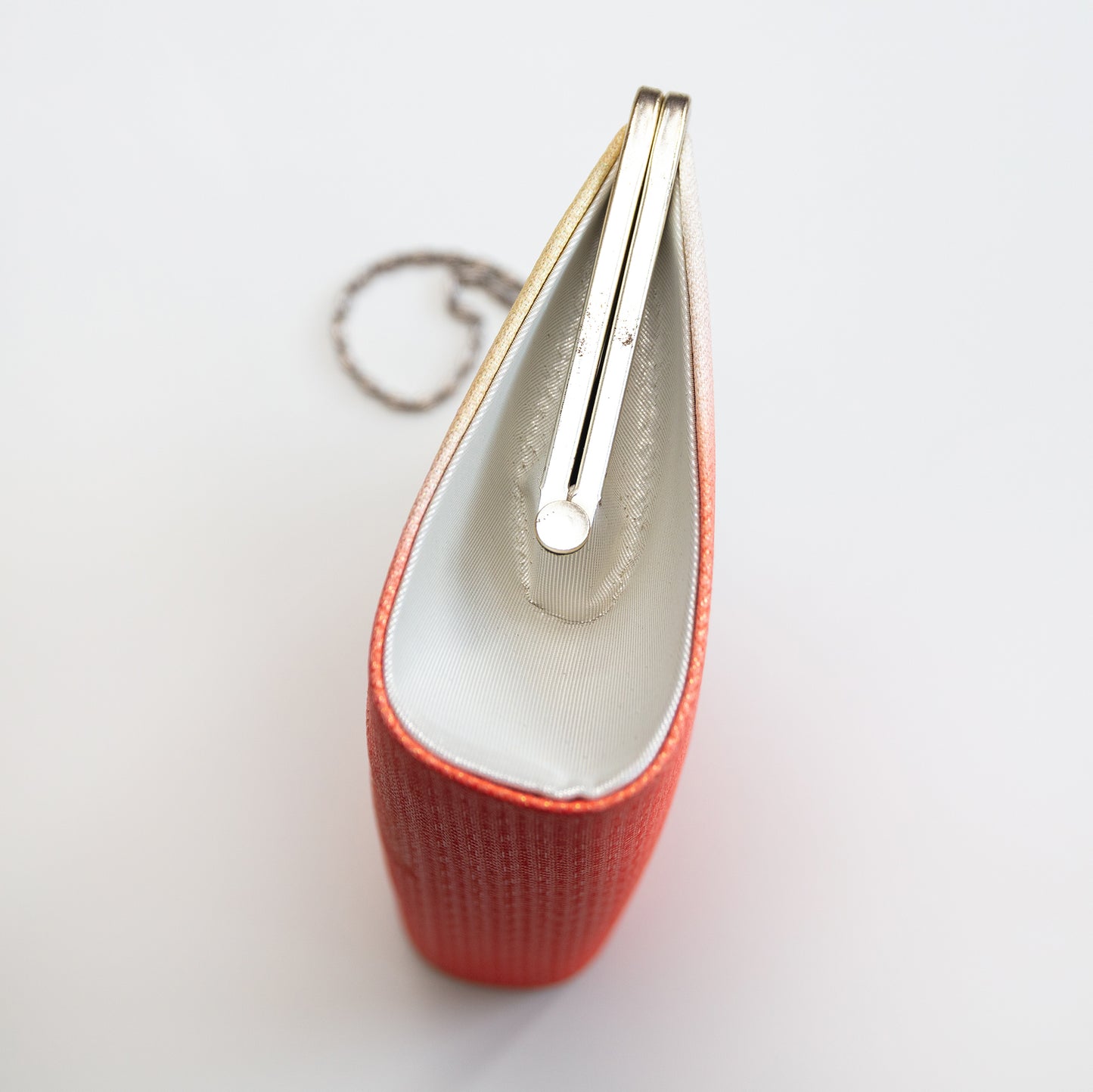 Side view of the vintage Japanese clutch bag with silver frame and chain and silver silk side panel on white background