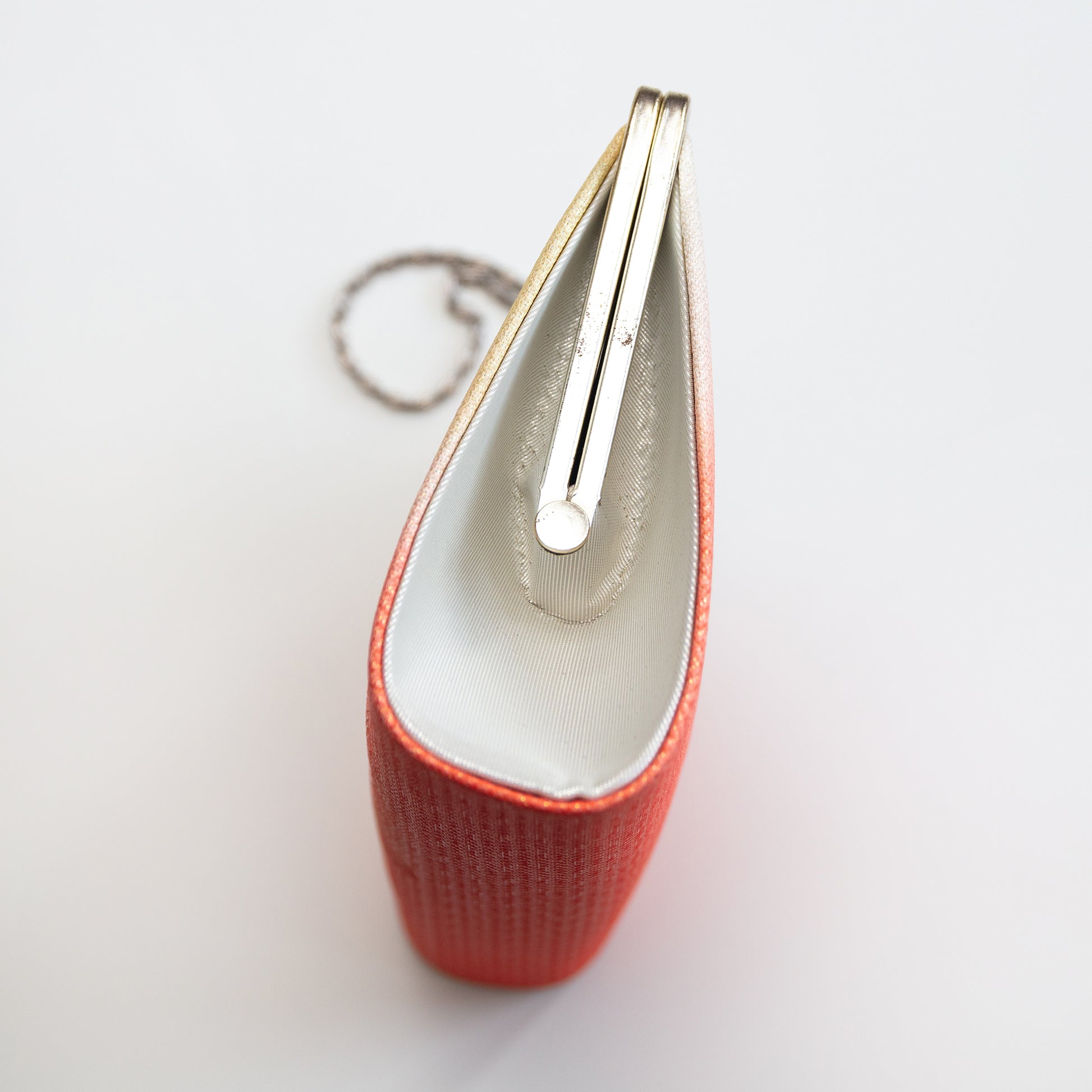 Side view of the vintage Japanese clutch bag with silver frame and chain and silver silk side panel on white background