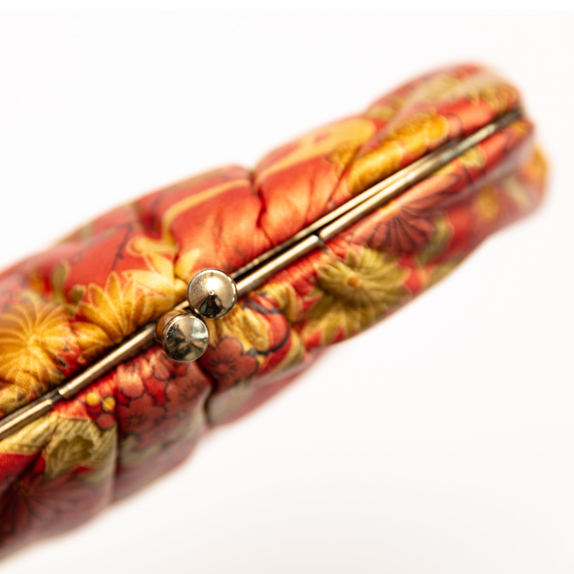 Close up of an orange leather floral clutch bag with gold clasp fastening on white background.
