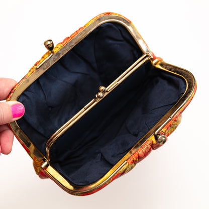 Decorative handbag with a floral pattern held open by a hand on a white background