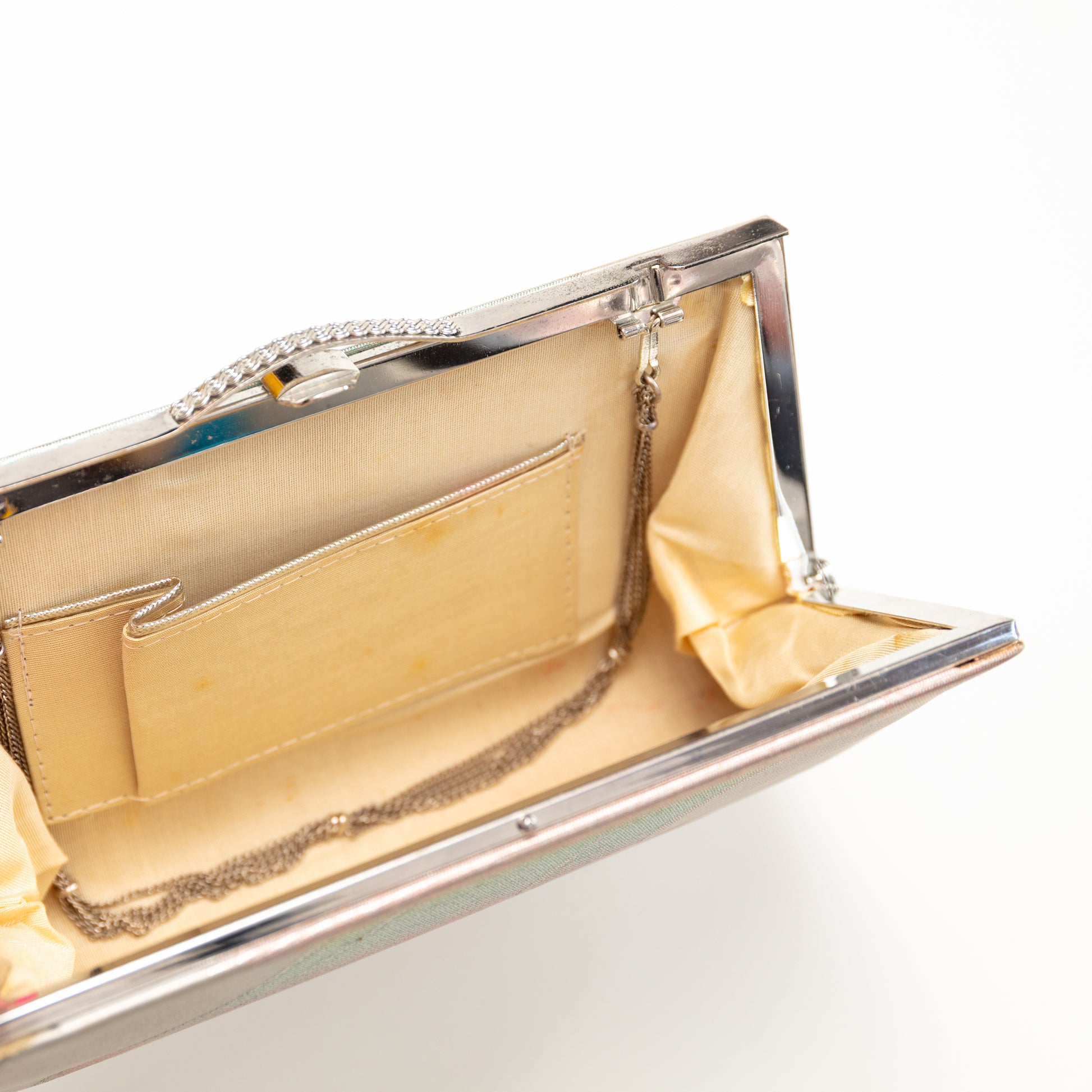 Close-up of a silver clutch with gold interior on a light gray background. The strap hinges tuck inside the bag if you want to use it without the strap.