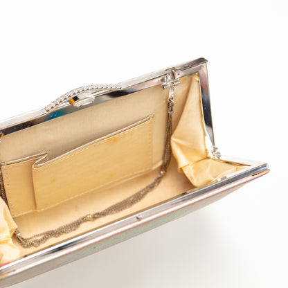 Close-up of a silver clutch with gold interior on a light gray background. The strap hinges tuck inside the bag if you want to use it without the strap.