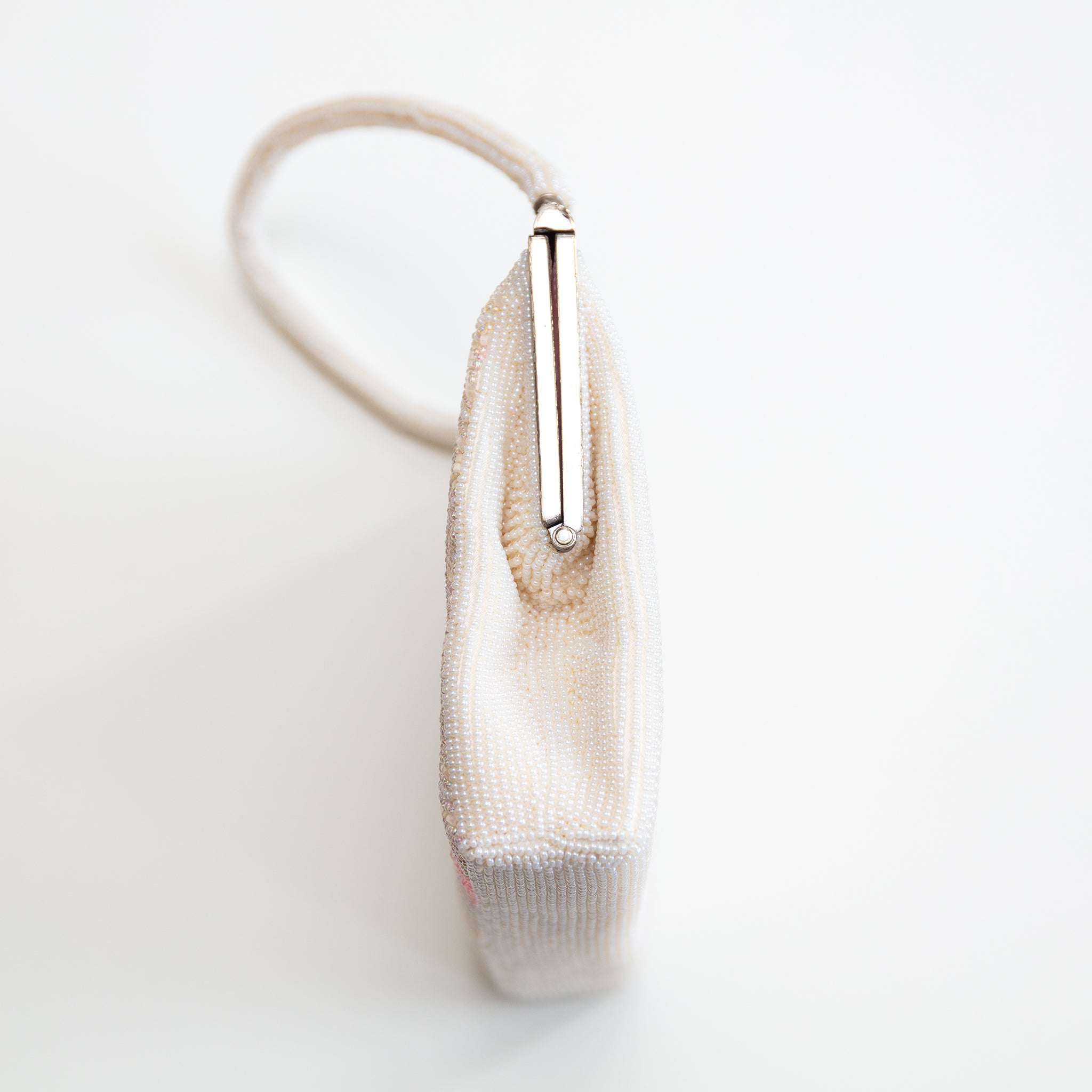 Close-up of pink and white beadwork pattern highlighting intricate embroidery and shimmering texture along the bag's upper