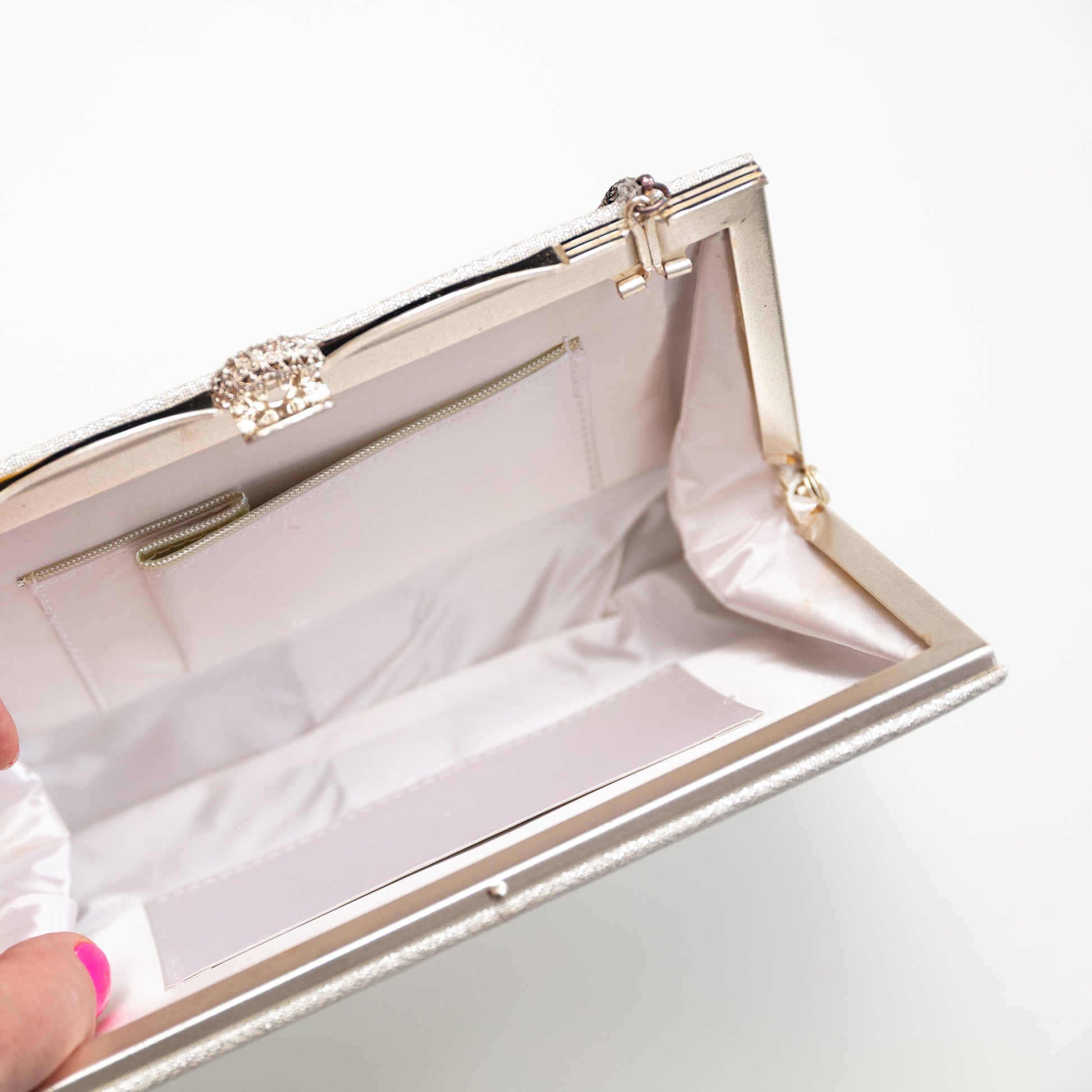Close-up of a silver and white clutch with a decorative clasp on a white background. The hinges old in or out depending on if you want to use the chain strap or not.