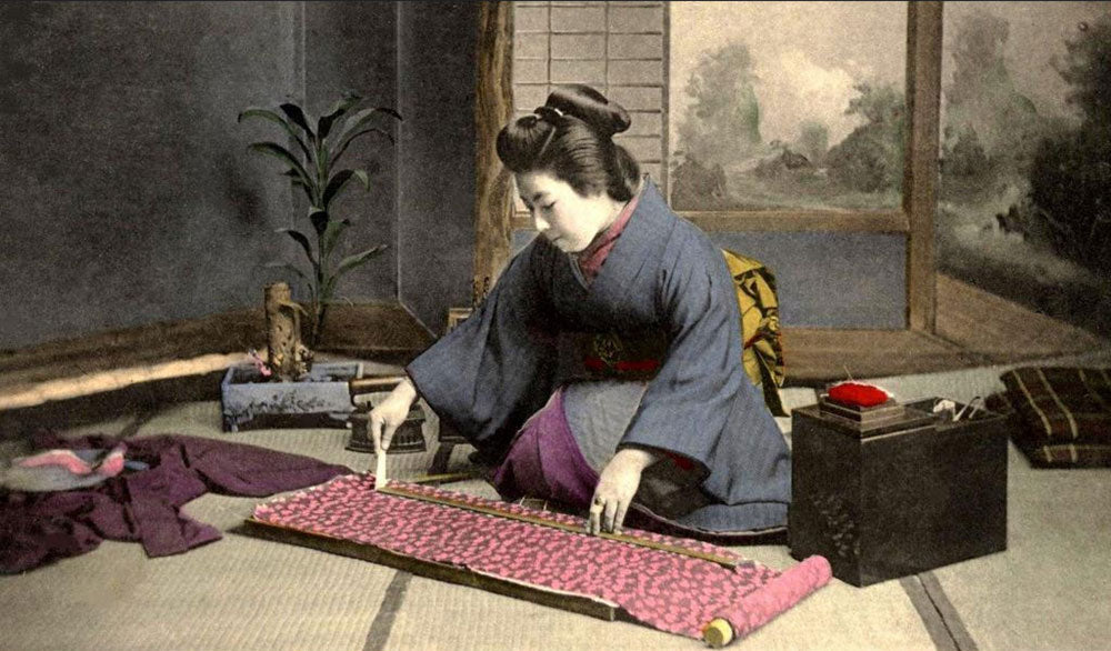 Vintage Japanese hand coloured photo of a woman in kimono measuring kimono silk on the floor.