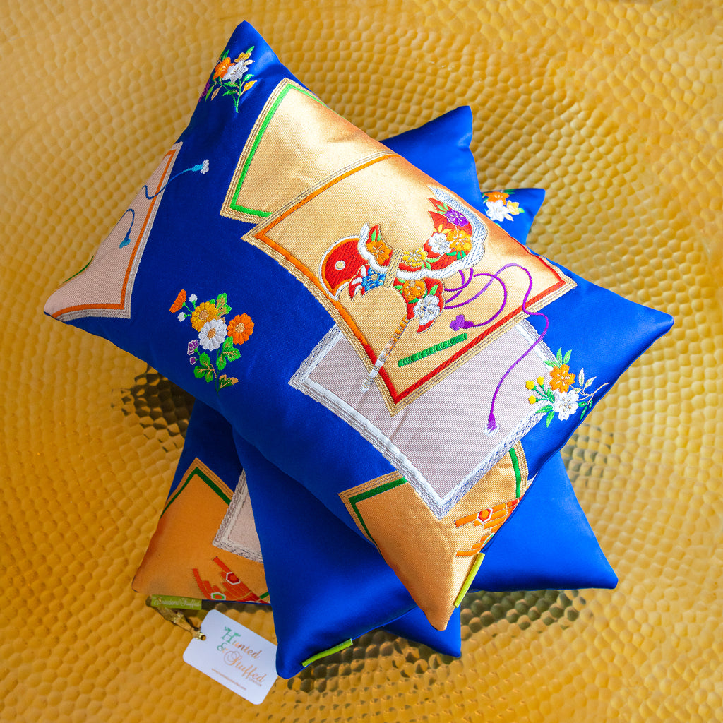 Close-up of gold accent obi cushions' textured metallic embroidery with plush electric blue fabric edges, highlighting