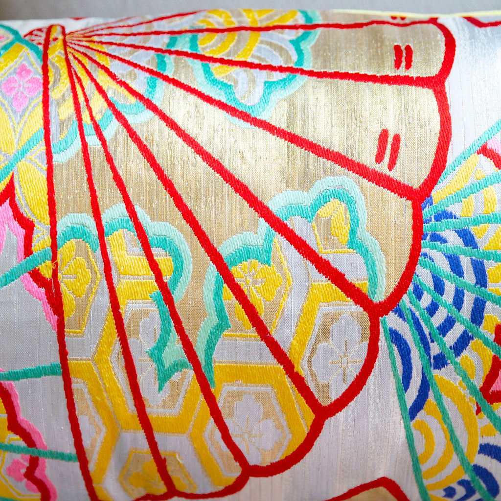Close-up of golden yellow fabric with detailed embroidery of oriental fans on shimmering silver Kimono silk bolster cushion