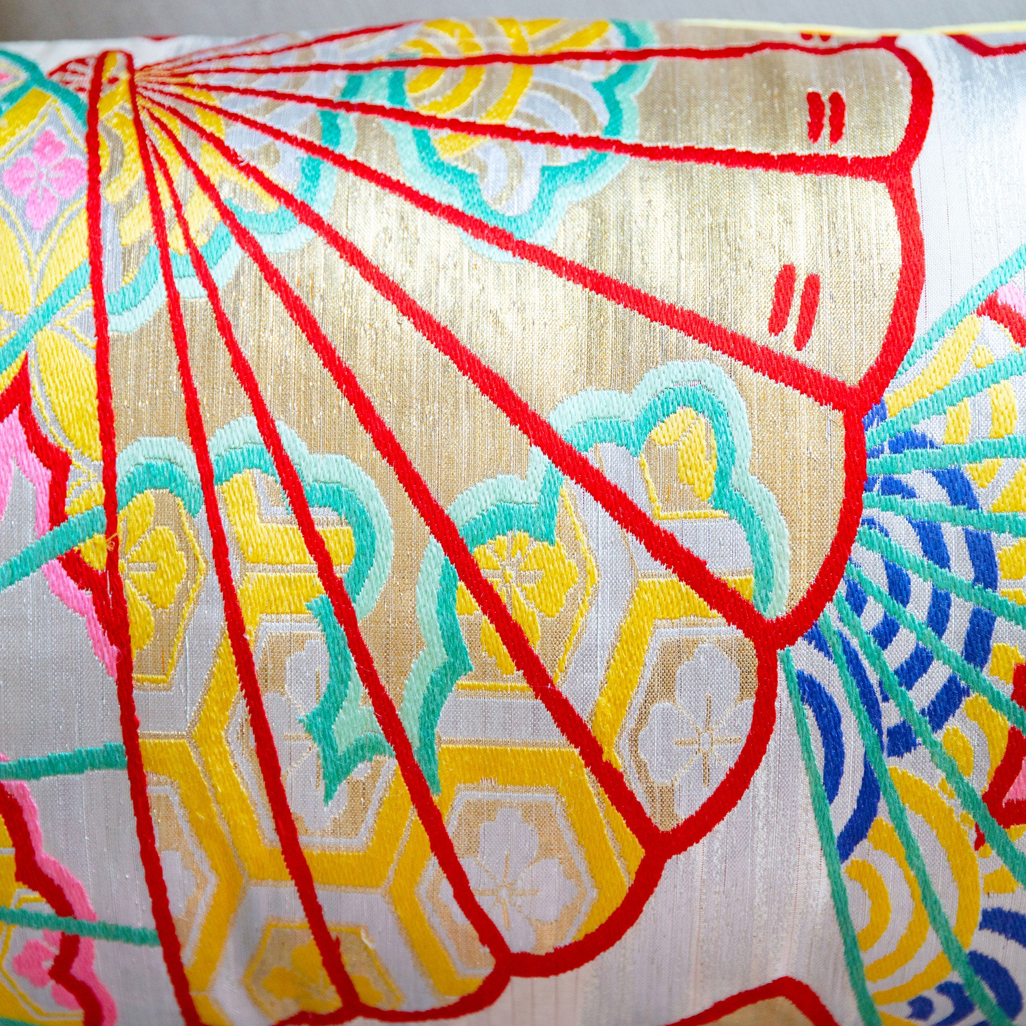 Close-up of golden yellow fabric with detailed embroidery of oriental fans on shimmering silver Kimono silk bolster cushion
