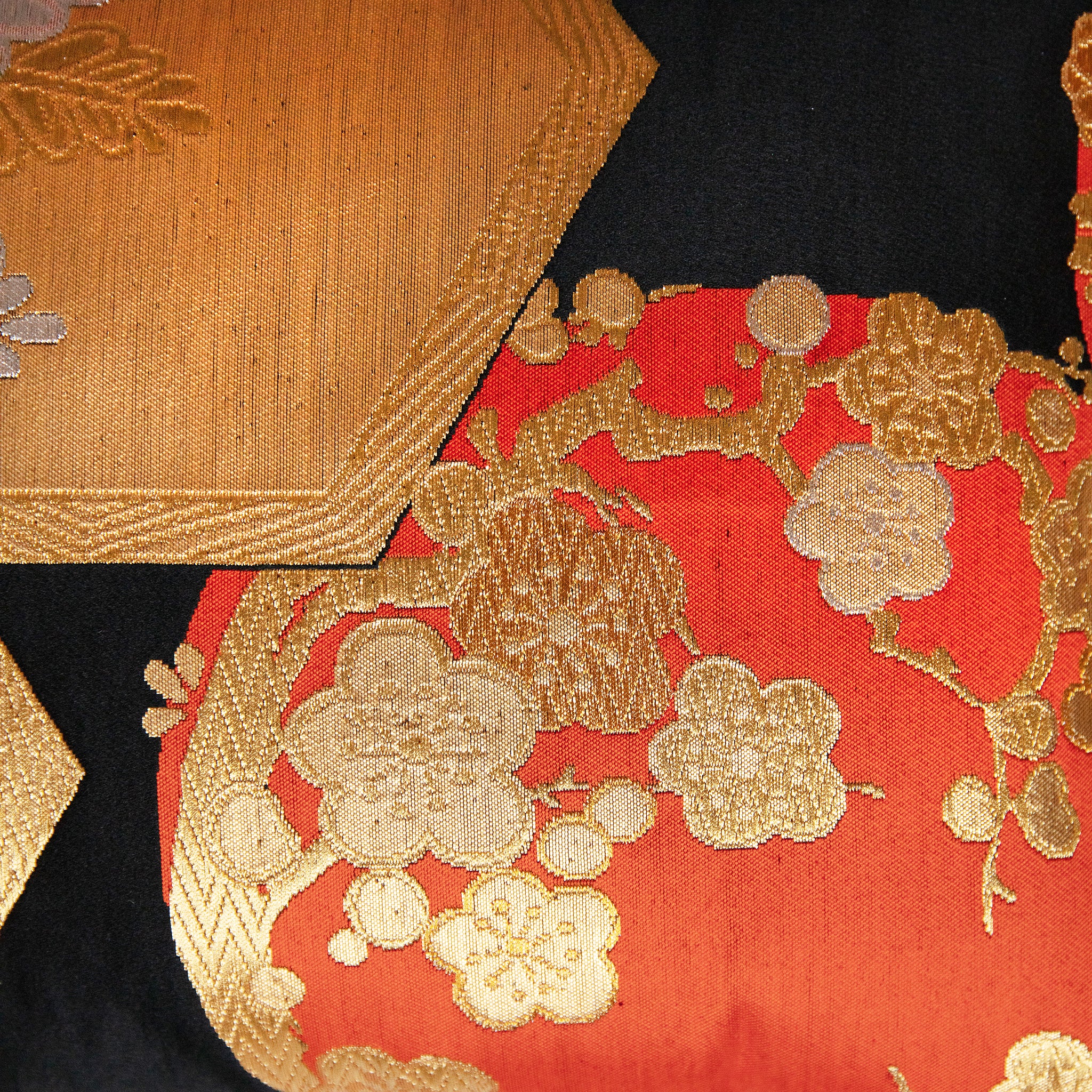 Close-up of black, gold, and orange silk fabric showcasing intricate Chinoiserie floral patterns and textured embroidery