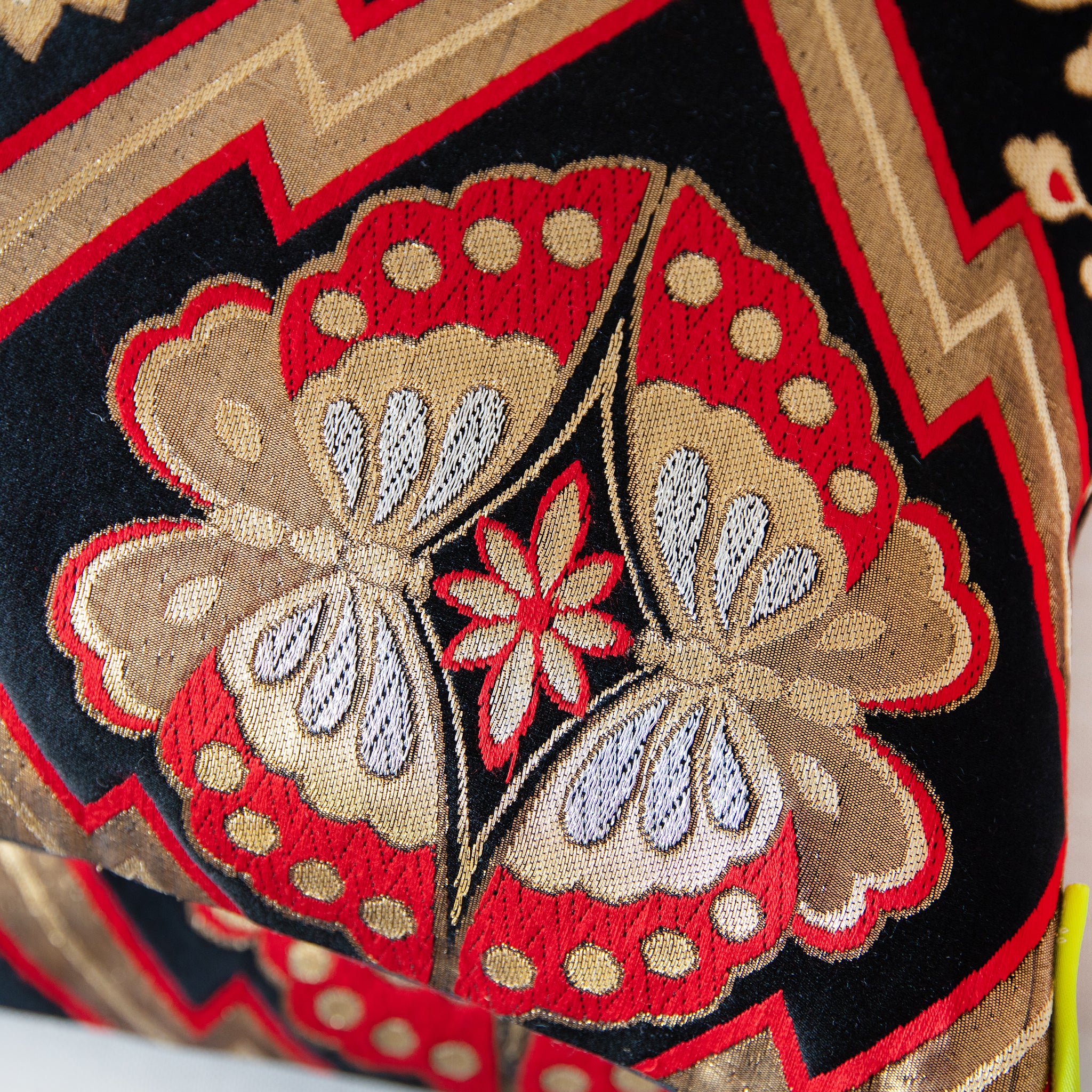 Close-up of intricate gold and red embroidery detailing on the metallic obi cushion’s textured silk fabric at a slight angle.