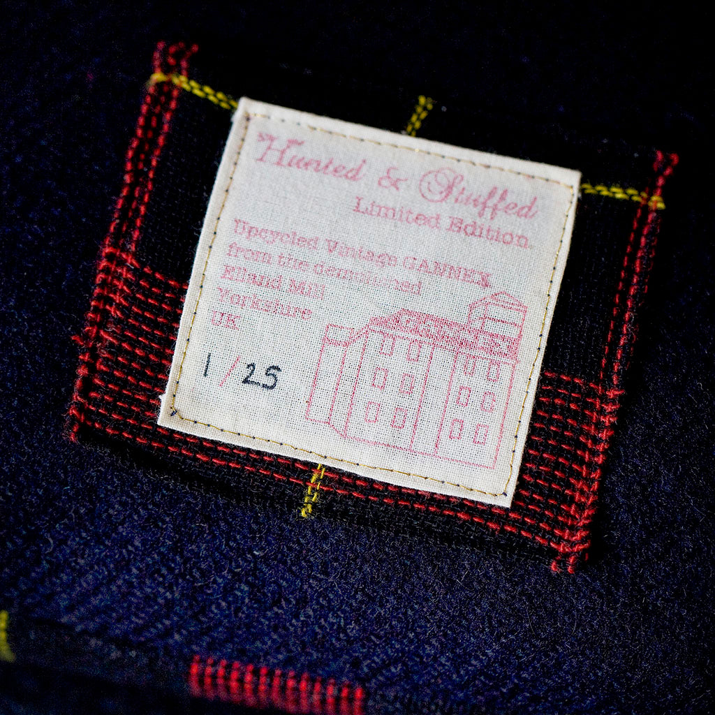 Close-up of the navy tartan pattern’s textured wool fibers and subtle vintage Gannex Ltd. branding detail on the cushion's