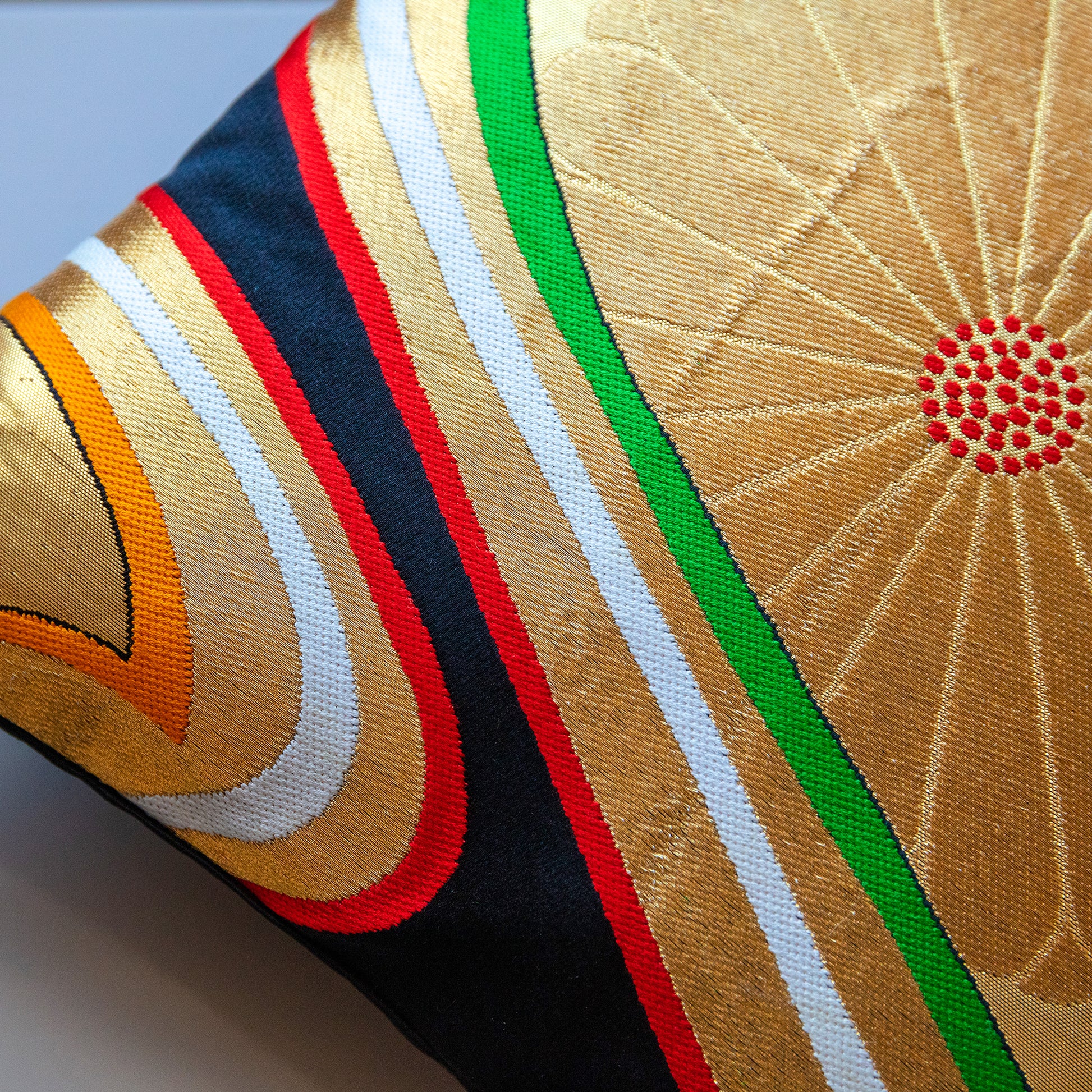 Detail of a corner of a black throw pillow with gold flowers and colourful accents. Vintage obi cushion.