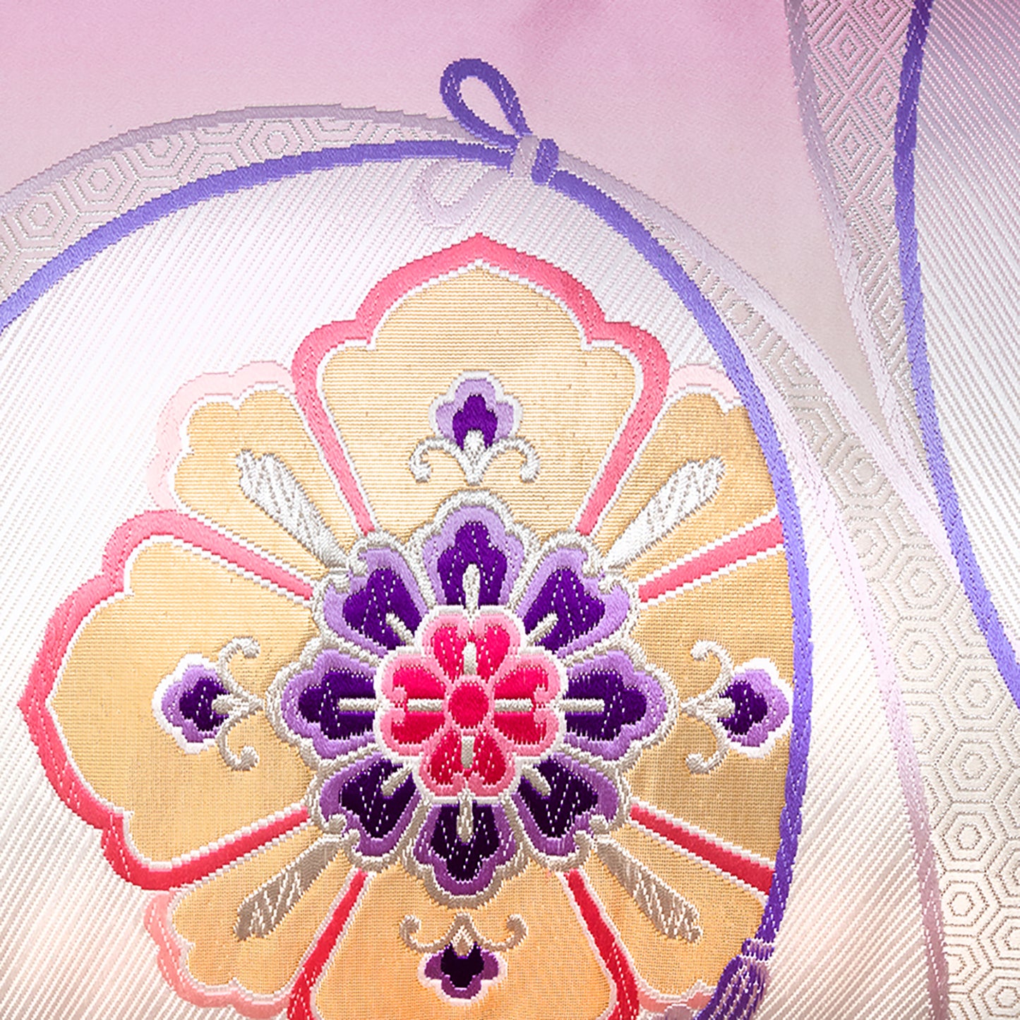 Detail of obi pillow, gold hanabishi flower with purple accents on cream silk