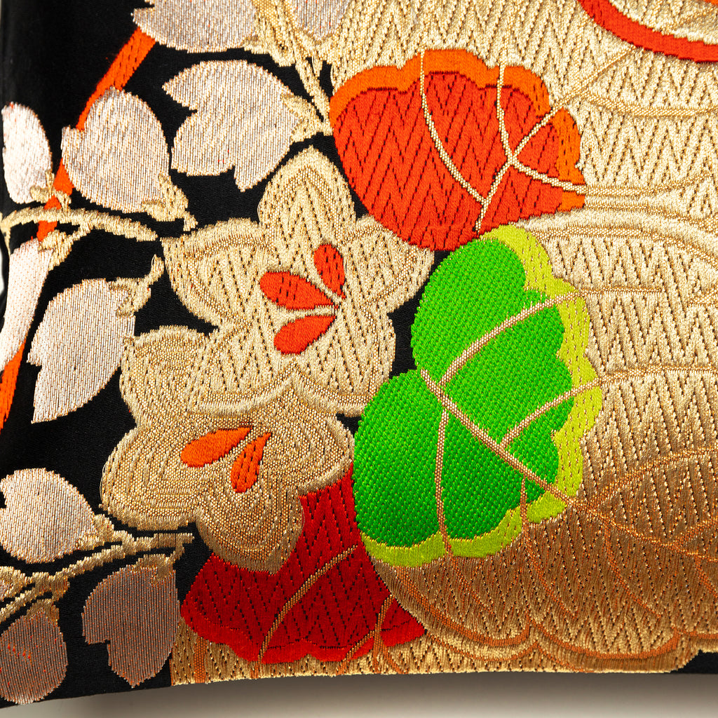 Close-up of orange and green embroidered accents on black silk Obi pillow fabric, highlighting intricate stitching details.