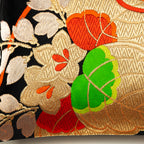Close-up of orange and green embroidered accents on black silk Obi pillow fabric, highlighting intricate stitching details.