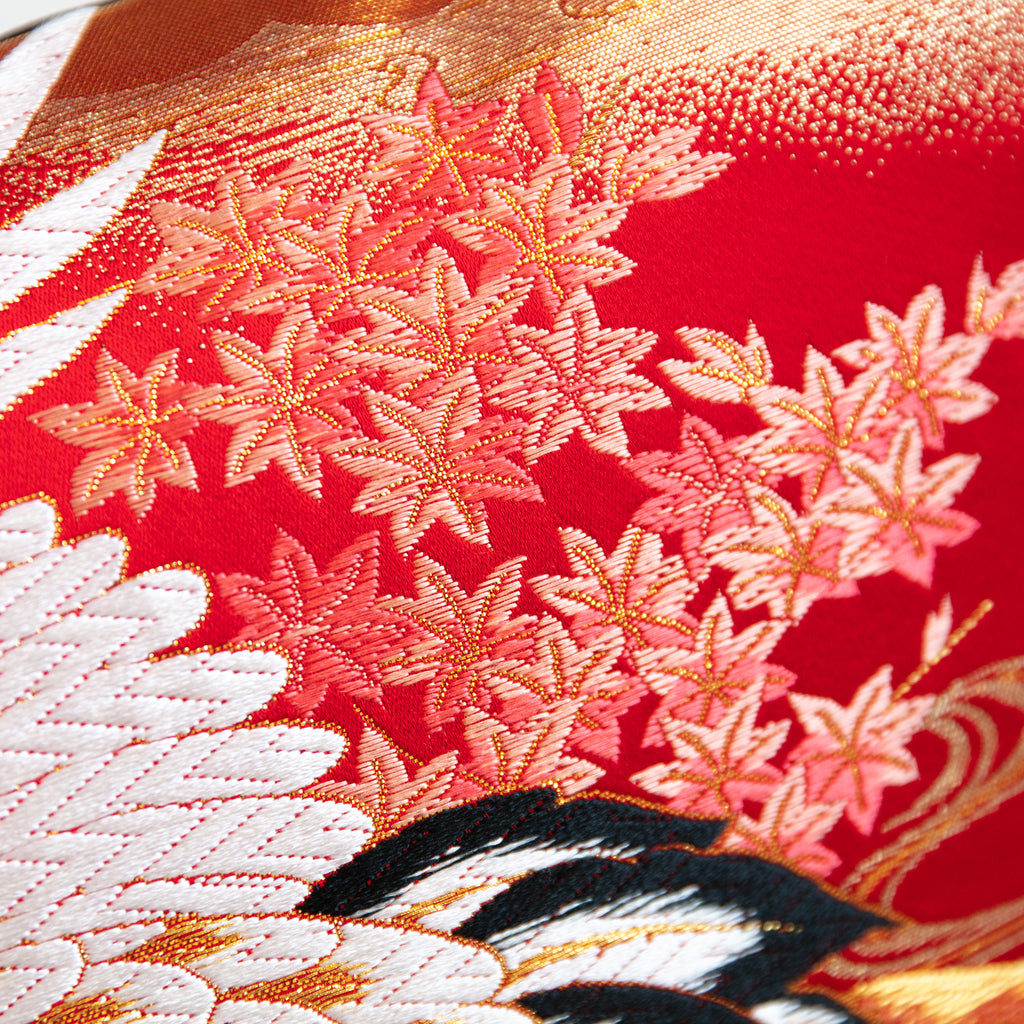 Close-up of vibrant red silk embroidery on black velvet, highlighting intricate crane feather details and textured surface.