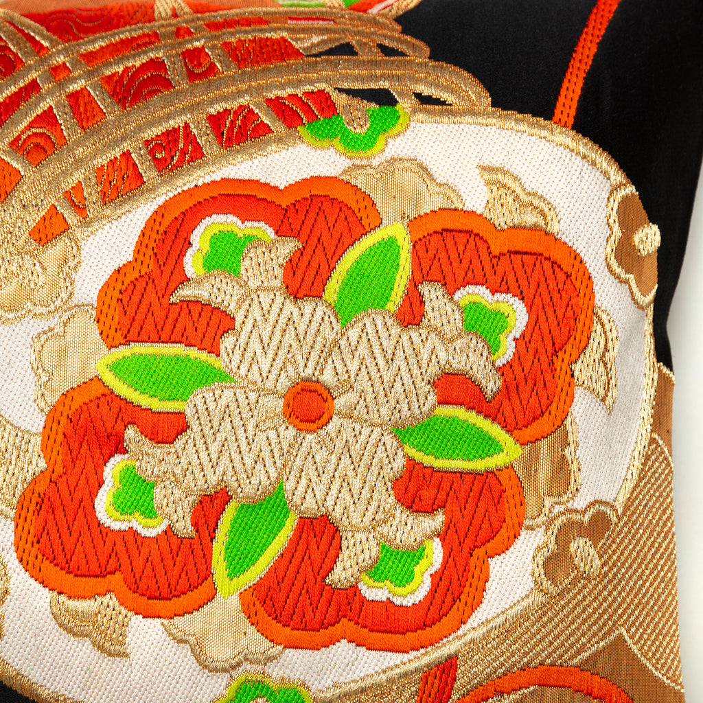 Close-up of the textured black silk fabric with orange and green embroidered accents on the Golden Drum Obi Pillow, showing