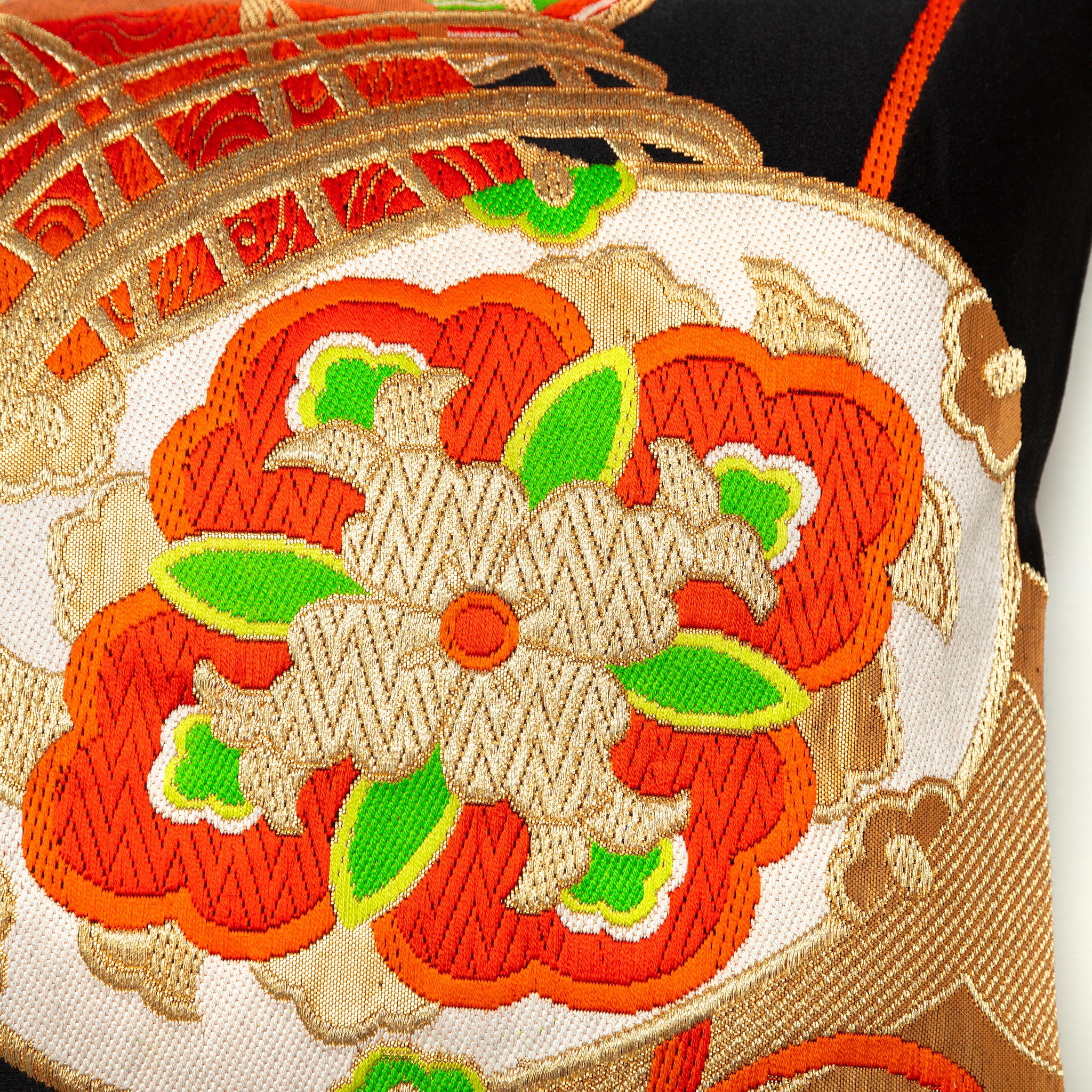 Close-up of the textured black silk fabric with orange and green embroidered accents on the Golden Drum Obi Pillow, showing