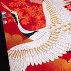 Close-up of red silk flying cranes embroidery detail on black velvet cushion surface, showcasing intricate stitching and