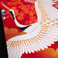 DEtail of flying crane cushion, close up of birds head and open wings over red silk