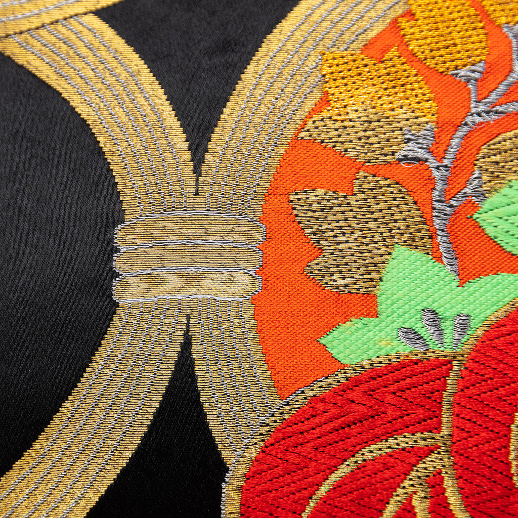Close-up of red gold pine tree embroidery on black velvet cushion fabric showing intricate needlework and textured surface.