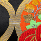 Close-up of red gold pine tree embroidery on black velvet cushion fabric showing intricate needlework and textured surface.