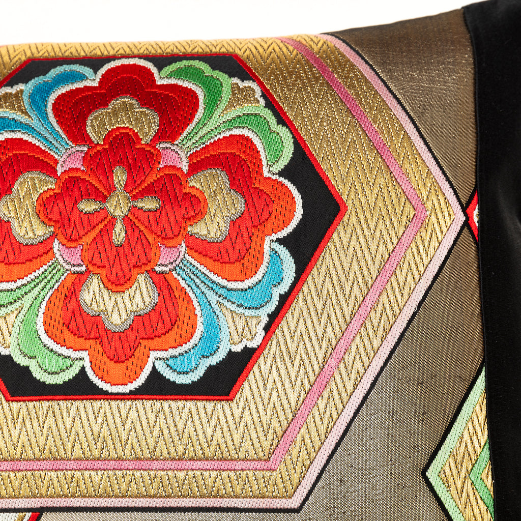 Close-up of gold hexagon embroidery detail on black silk cushion surface, highlighting textured metallic thread and precise