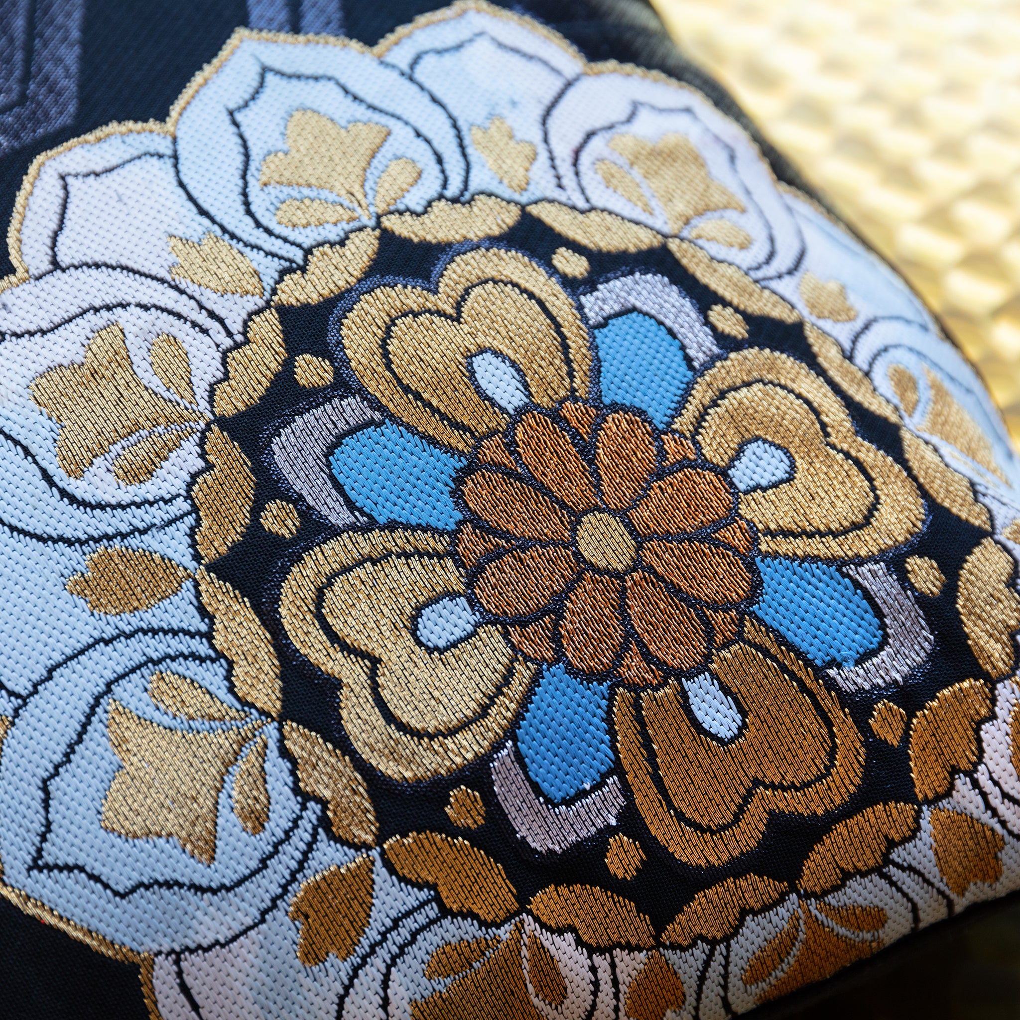 Close-up of red and blue embroidered floral details on textured black silk fabric of the Obi pillow from an overhead