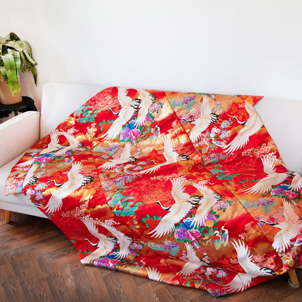 Close-up of textured red silk fabric showing intricate vintage kimono-inspired embroidery detail on the throw blanket
