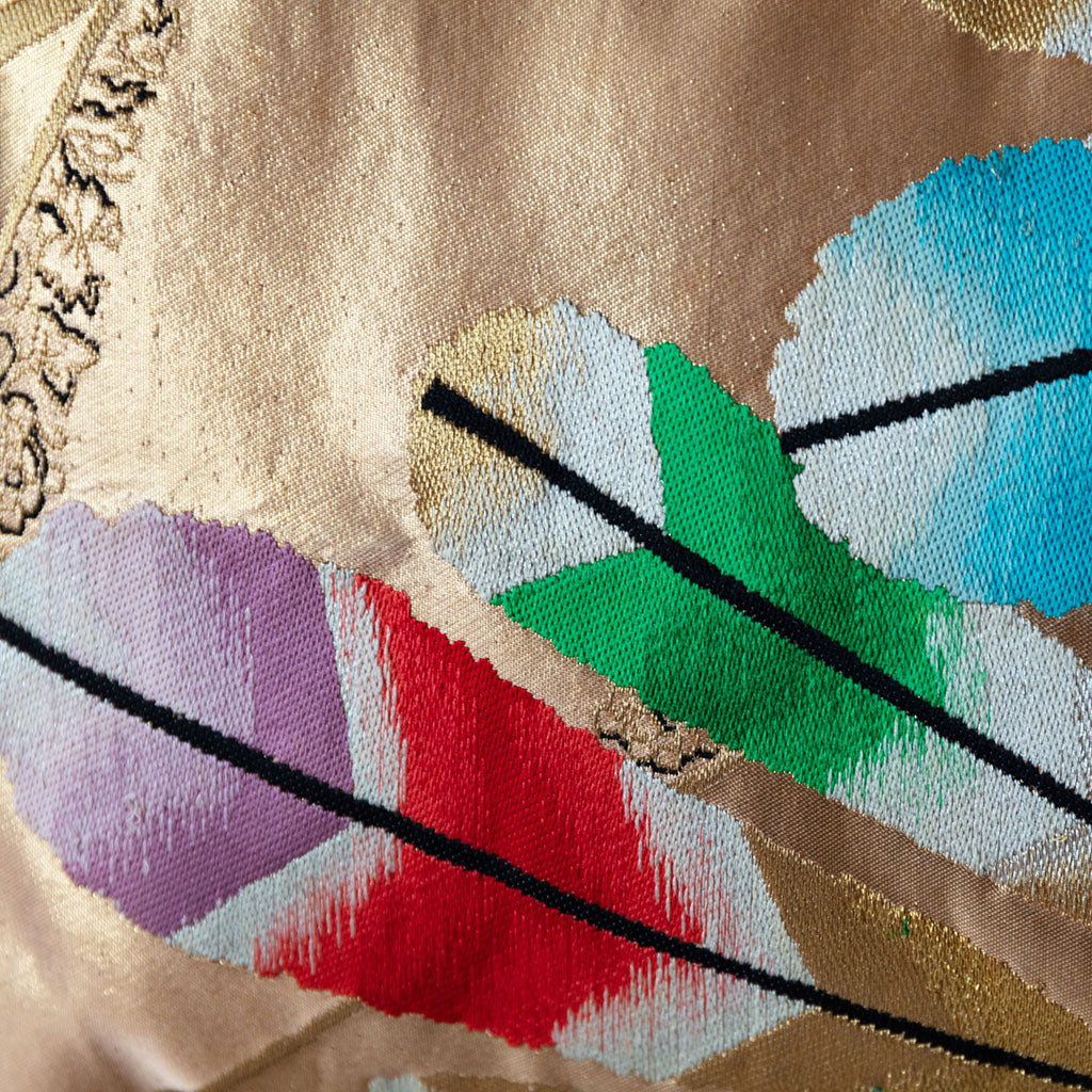 Close-up of the gold metallic gilt feather embroidery highlighting textured silk fabric and intricate detailing on the