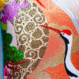 Close up of the orange wedding kimono pillow showing the crane's head and beak and an abstract bronze woven pattern silk.