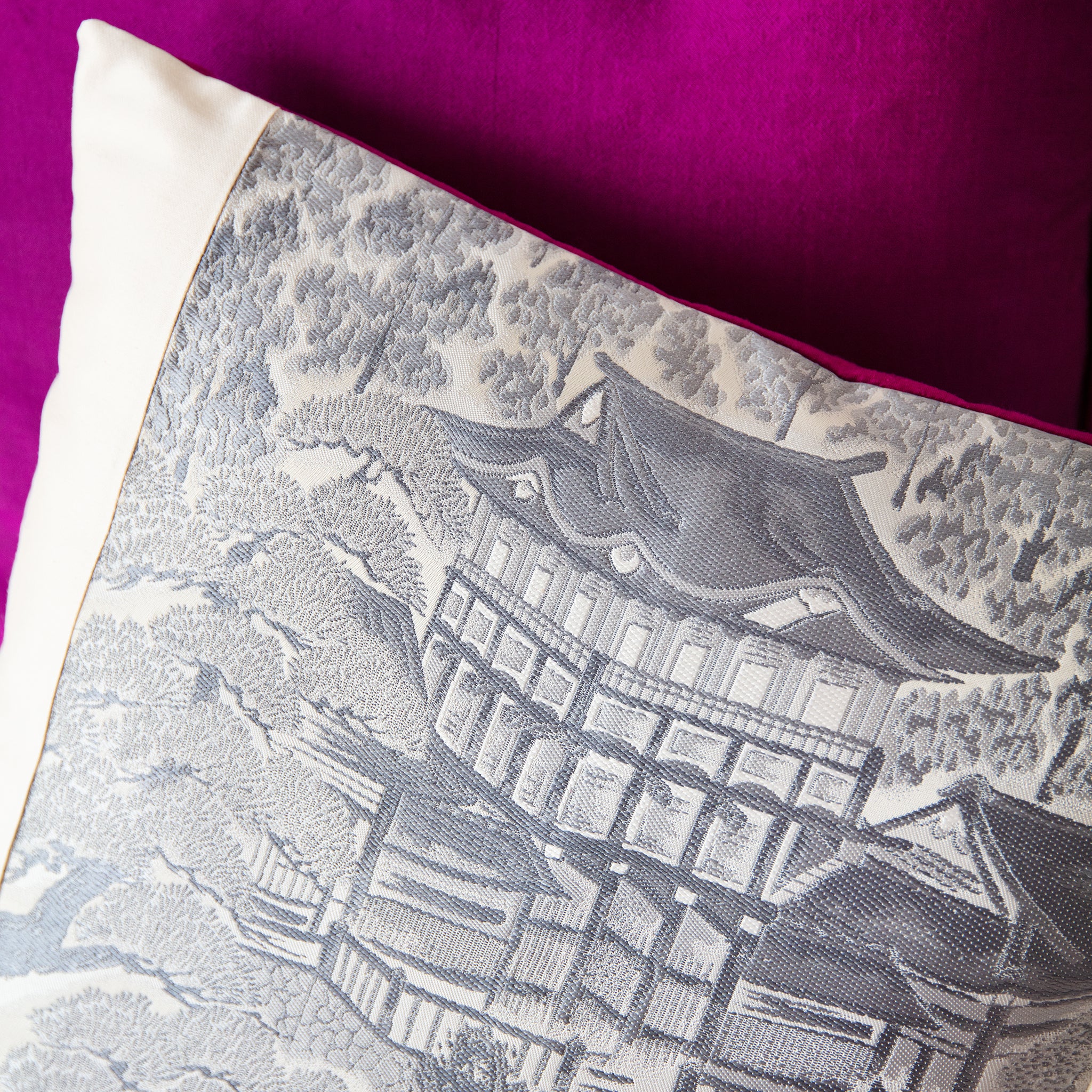 Close-up of grey silk texture with visible stitching along the cushion edge and hints of the Shocking Pink silk backing.