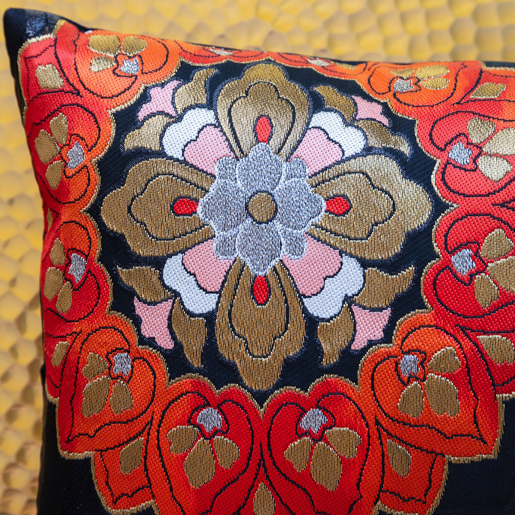 Close-up of the red and blue floral embroidered patterns on the textured black silk surface of the Obi pillow fabric