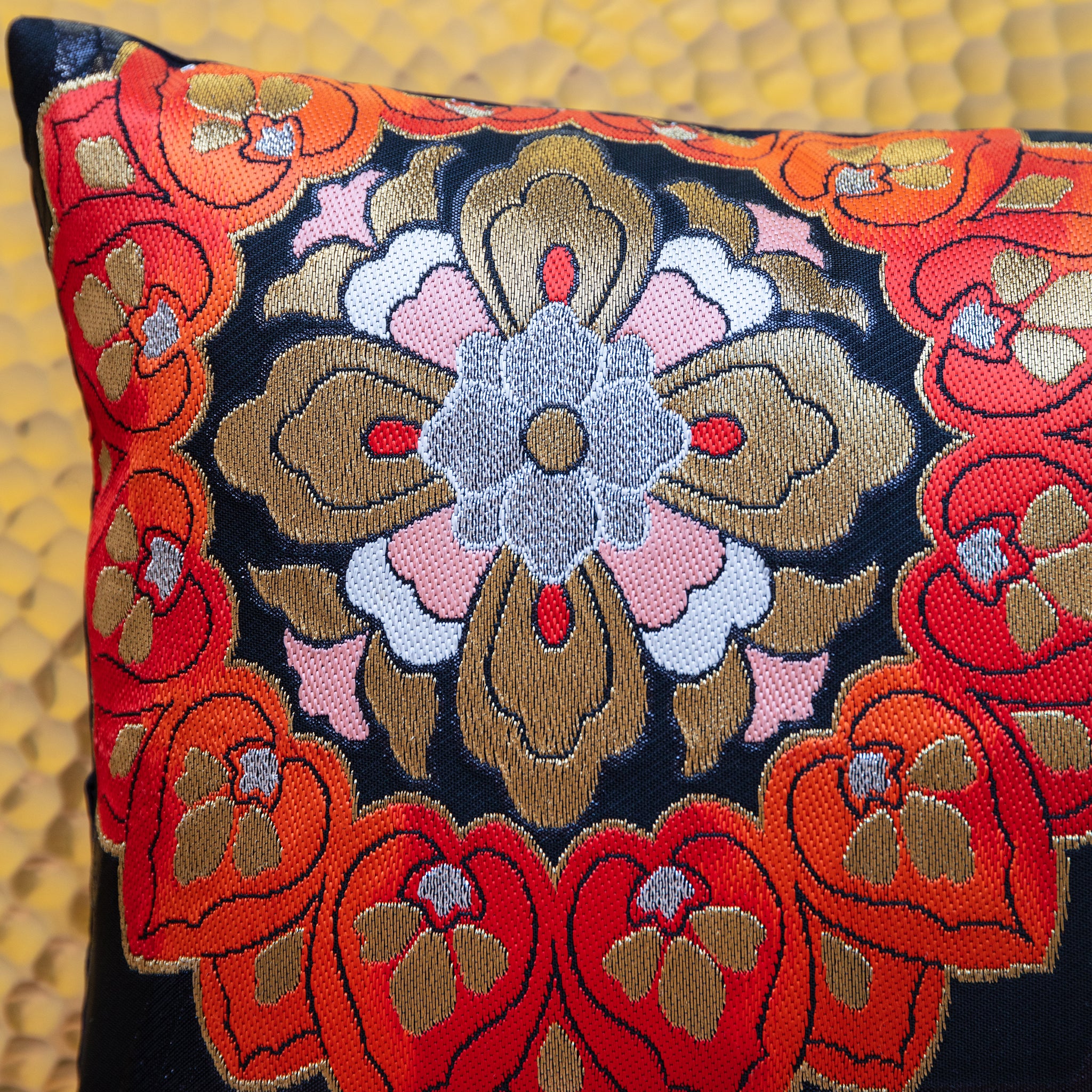Close-up of the red and blue floral embroidered patterns on the textured black silk surface of the Obi pillow fabric