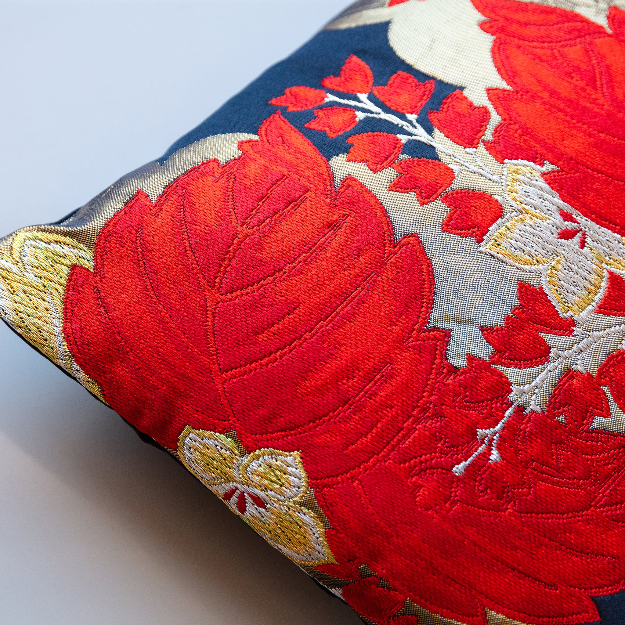 Close-up of vibrant red and gold floral embroidery detail on black silk pillow fabric displaying intricate stitching and