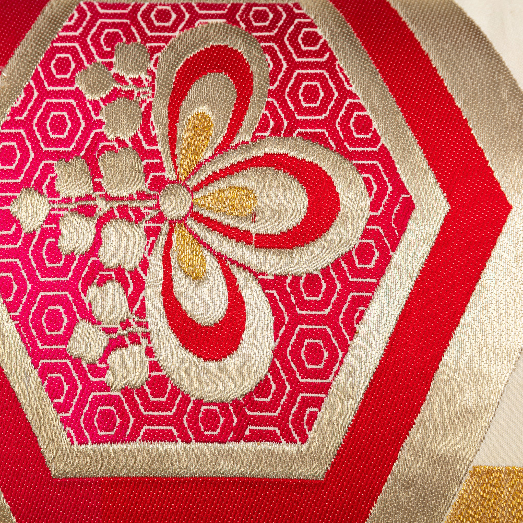 Close-up of cream silk obi pillow fabric showing vibrant red hexagon Kiri flower pattern and intricate embroidered details