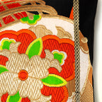 Close-up of the Golden Drum Obi Pillow’s textured black silk fabric with vibrant orange and green embroidered accents along